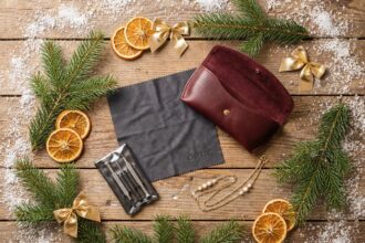 Accessoires pour lunettes disposés en flat lay sur une table en bois décorée pour Noël : étui en cuir bordeaux, chiffon microfibre, kit de réparation et chaîne porte-lunettes