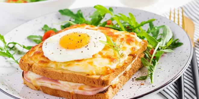Croque madame sandwich and a cup of latte macchiato coffee on the table.