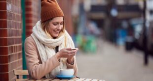 Female Customer Sending Text Message Sitting Outside Coffee Shop On Busy City High Street In Fall