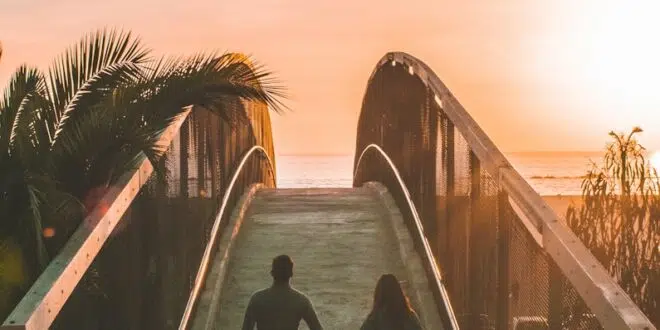 man and woman holding hand while walking on bridge