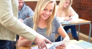 Smiling female student with digital tablet and teacher in classroom