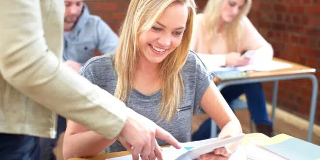 Smiling female student with digital tablet and teacher in classroom
