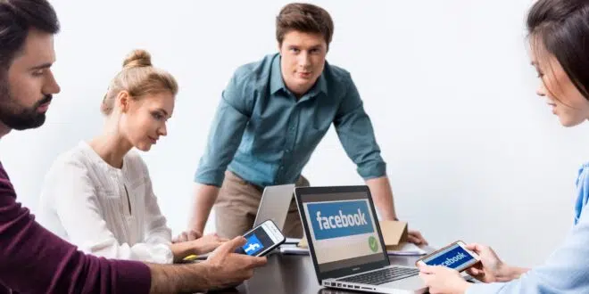 Young businesspeople using digital devices with facebook logo icons on screens